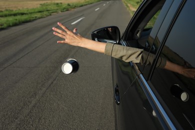 Photo of Driver throwing away paper cup from car window. Garbage on road