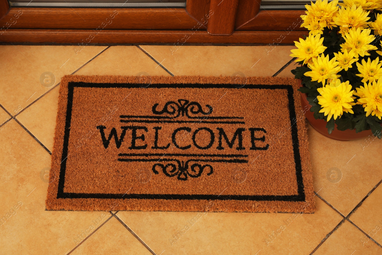 Photo of Door mat with word Welcome and beautiful flowers on floor near entrance