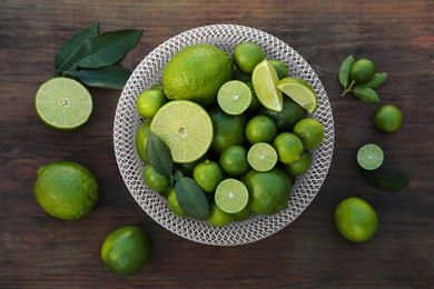 Photo of Fresh ripe limes and green leaves on wooden table, flat lay