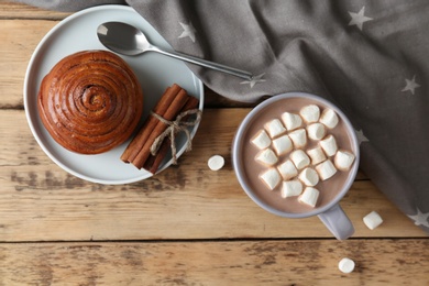 Composition with delicious hot cocoa drink and bun on wooden background, flat lay