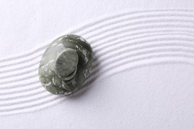 Photo of Zen garden stones on white sand with pattern, top view. Space for text