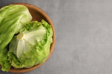 Photo of Bowl with fresh green iceberg lettuce head and leaves on grey table, top view. Space for text