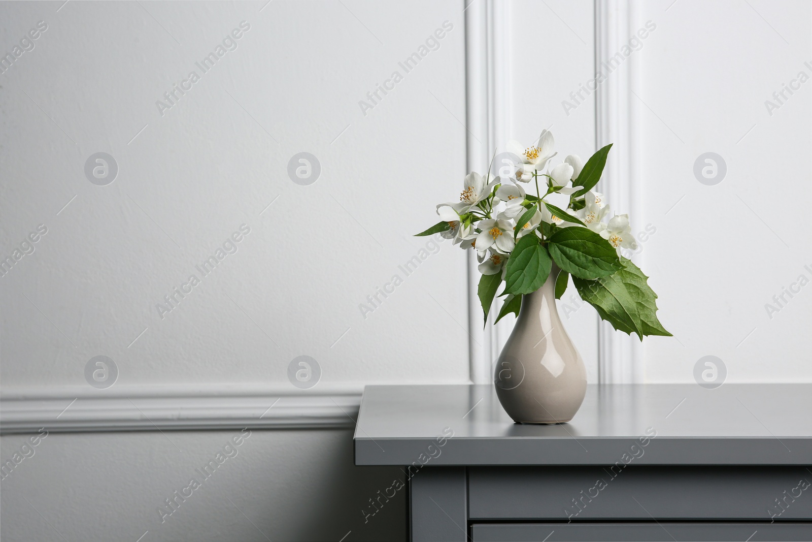 Photo of Beautiful bouquet with fresh jasmine flowers in vase on grey table indoors, space for text