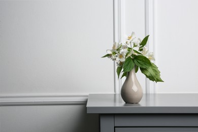 Photo of Beautiful bouquet with fresh jasmine flowers in vase on grey table indoors, space for text