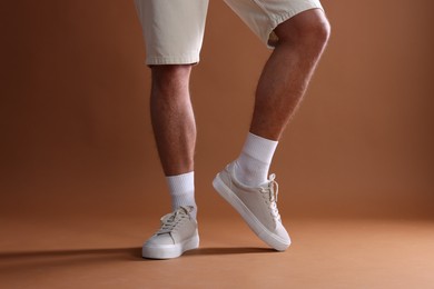Photo of Man wearing stylish sneakers on brown background, closeup