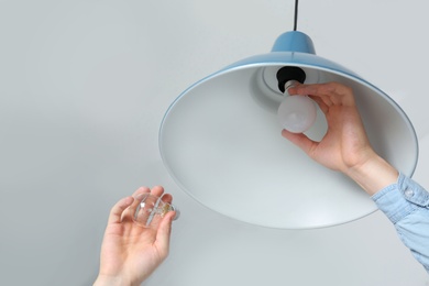 Man changing light bulb in pendant lamp on white background, low angle view