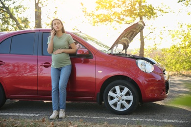 Stressed pregnant woman talking on phone near broken car outdoors