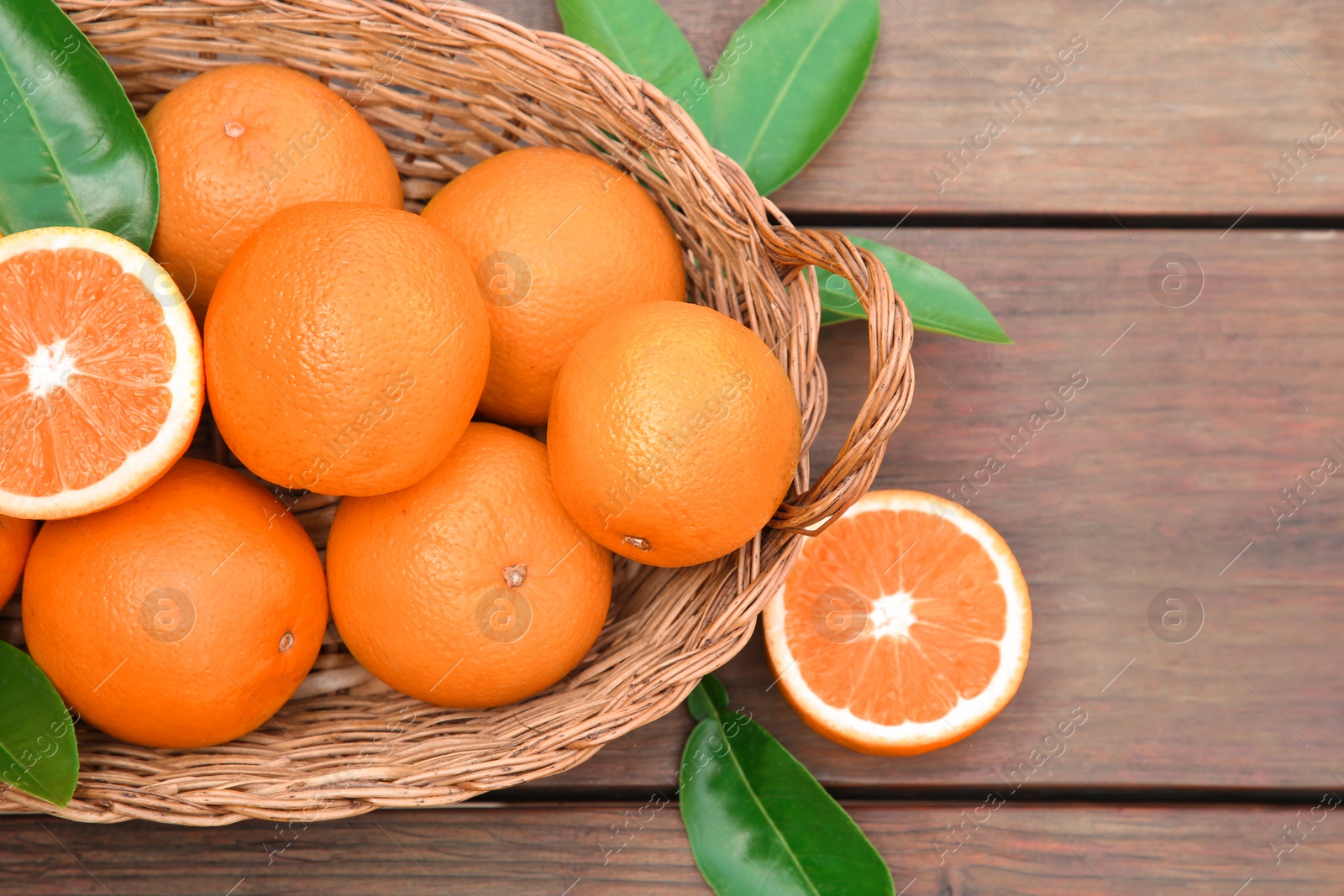 Photo of Wicker basket with ripe juicy oranges and green leaves on wooden table, flat lay. Space for text