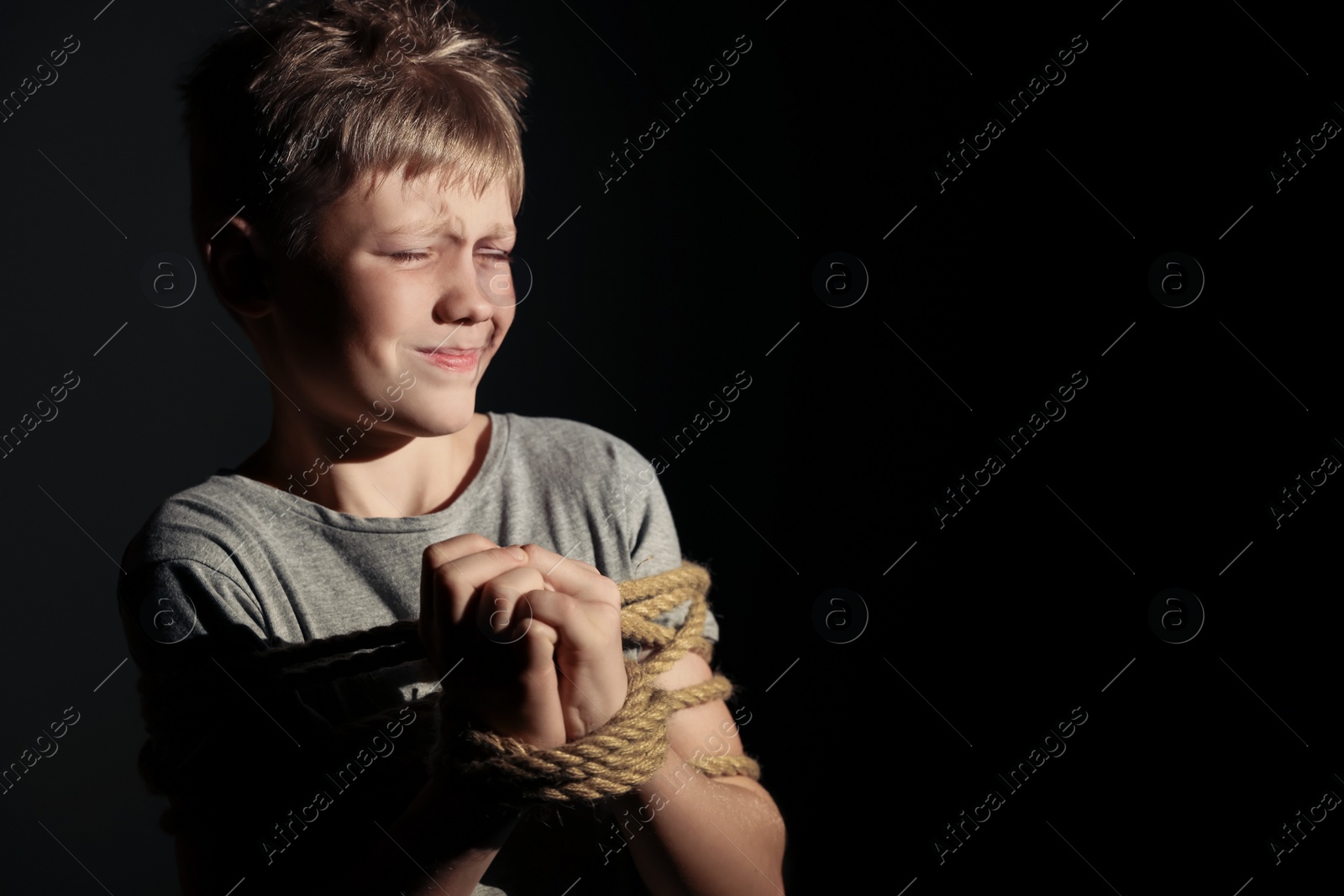 Photo of Little boy with bruises tied up and taken hostage on dark background. Space for text