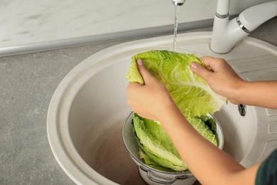 Photo of Woman washing leaf of savoy cabbage under tap water in kitchen sink, closeup