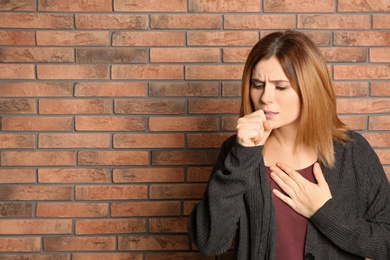 Woman suffering from cough near brick wall. Space for text