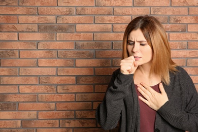 Photo of Woman suffering from cough near brick wall. Space for text