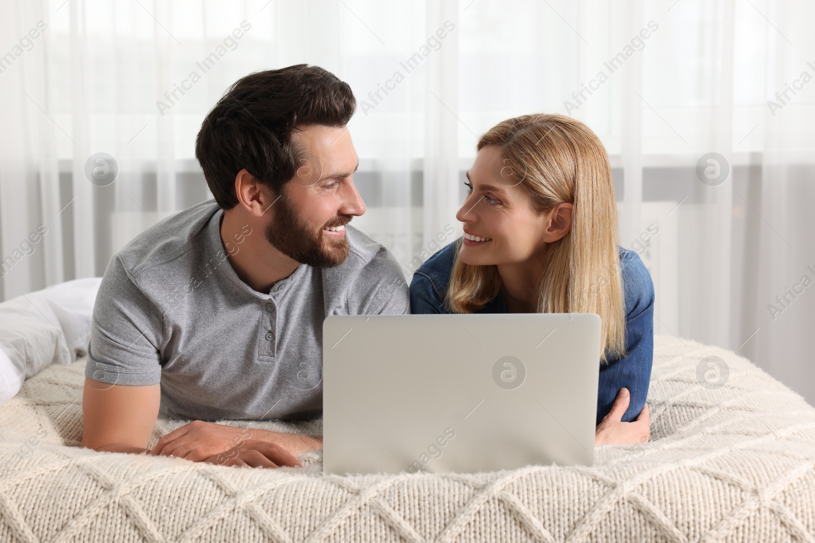 Photo of Happy couple with laptop on bed at home