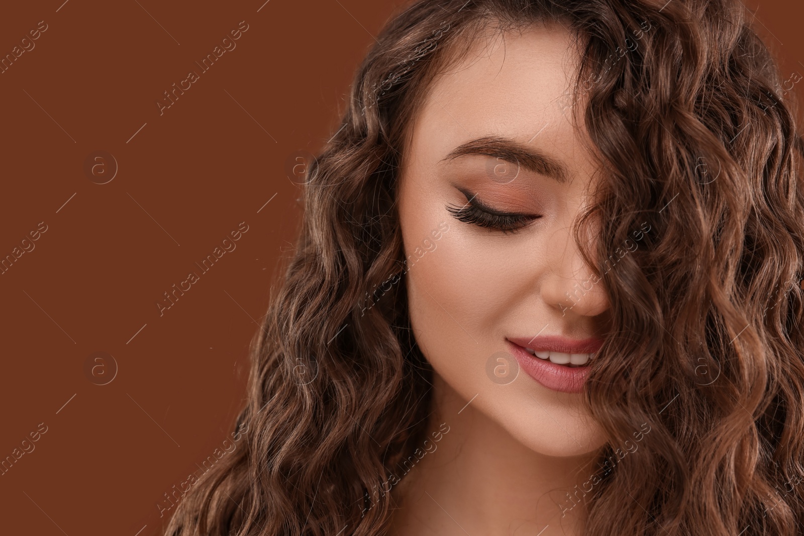 Photo of Beautiful young woman with long curly hair on brown background, closeup. Space for text