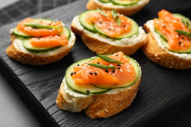 Tasty canapes with salmon, cucumber and cream cheese on grey table, closeup