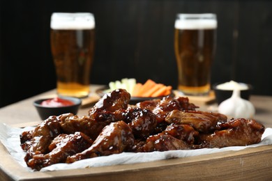 Photo of Tasty chicken wings served with beer on wooden table, closeup. Delicious snack