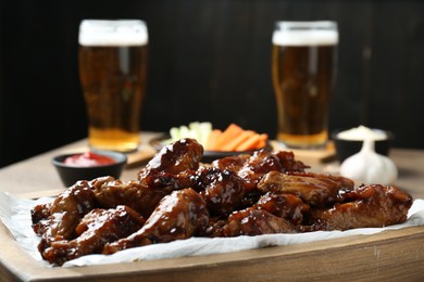 Tasty chicken wings served with beer on wooden table, closeup. Delicious snack