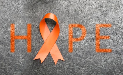 Image of Orange awareness ribbon and word HOPE on grey background, top view 