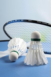 Feather badminton shuttlecocks and racket on blue table against blurred background, closeup