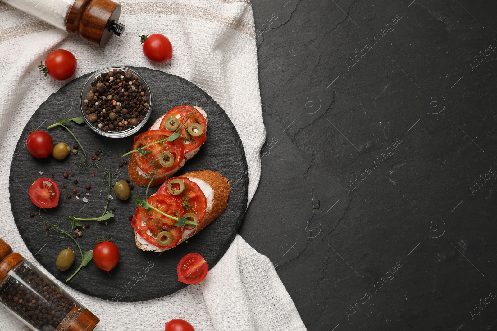 Photo of Delicious ricotta bruschettas with sliced tomatoes, olives and greens on black table, top view. Space for text