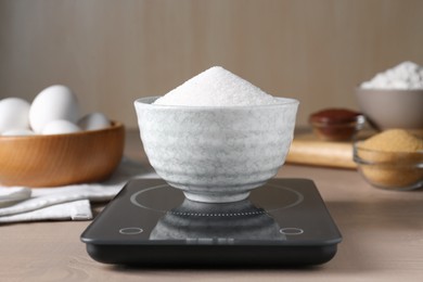 Photo of Electronic scales with sugar on light wooden table