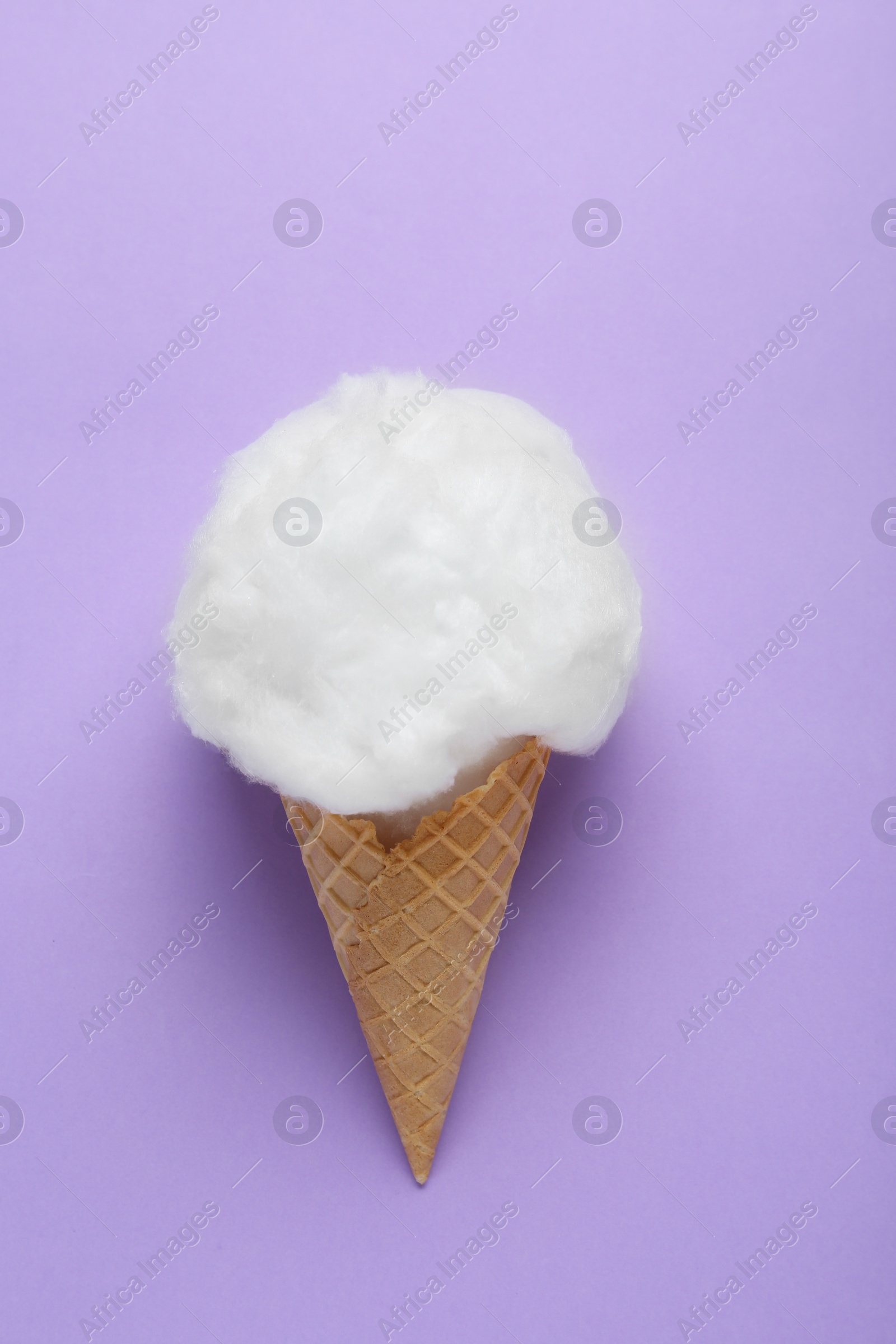 Photo of Sweet cotton candy in waffle cone on purple background, top view