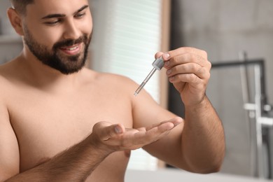 Photo of Young man applying cosmetic serum onto his hand in bathroom, selective focus