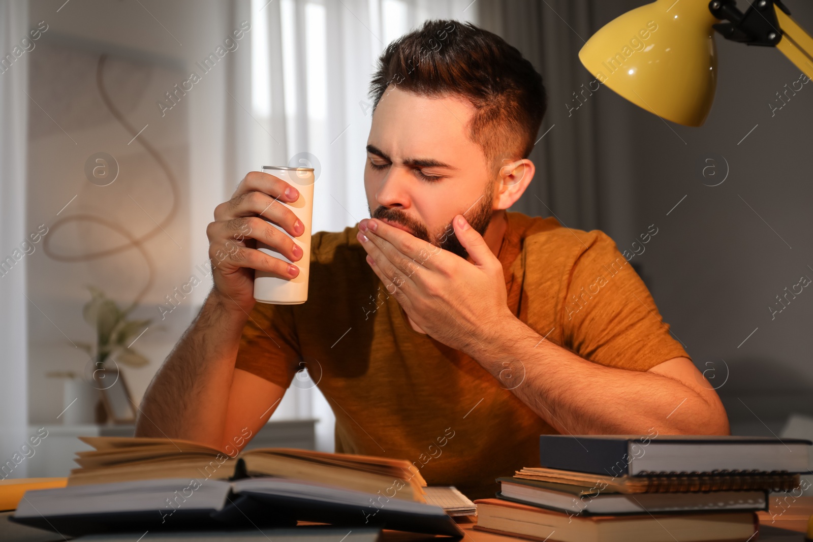 Photo of Tired young man with energy drink studying at home