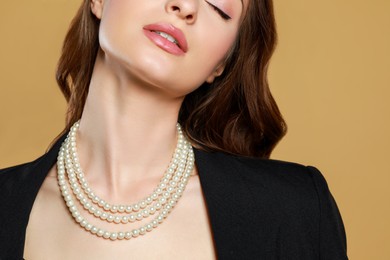 Photo of Young woman with elegant pearl necklace on brown background, closeup
