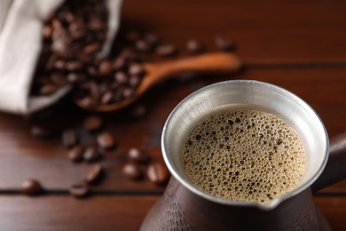 Photo of Turkish coffee in cezve on wooden table, closeup. Space for text