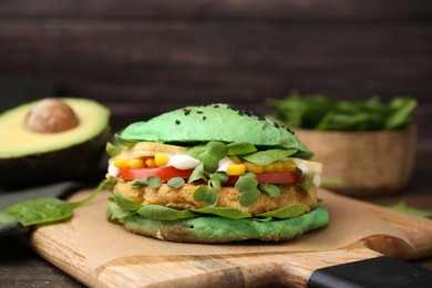 Photo of Tasty green vegan burger with vegetables, patty and microgreens on wooden table, closeup