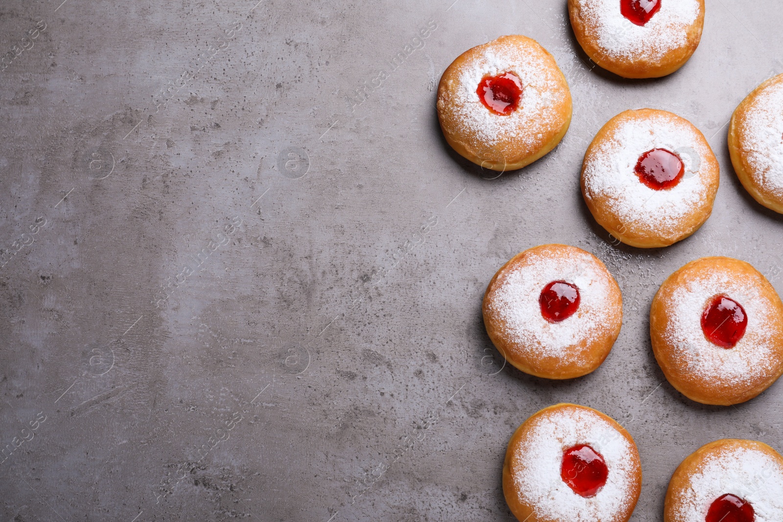 Photo of Hanukkah doughnuts with jelly and sugar powder on grey table, flat lay. Space for text