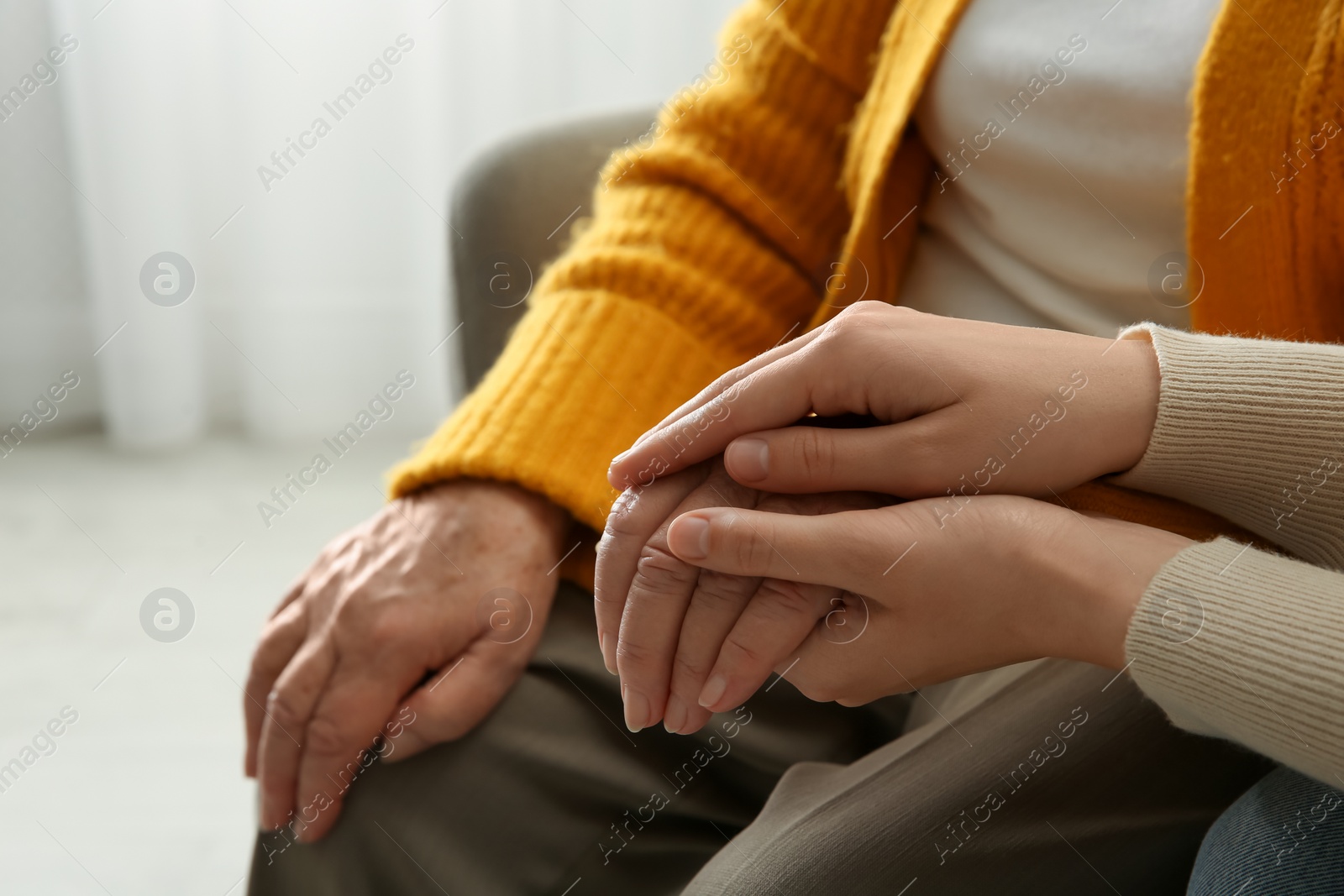 Photo of Young and elderly women holding hands together at home, closeup. Space for text