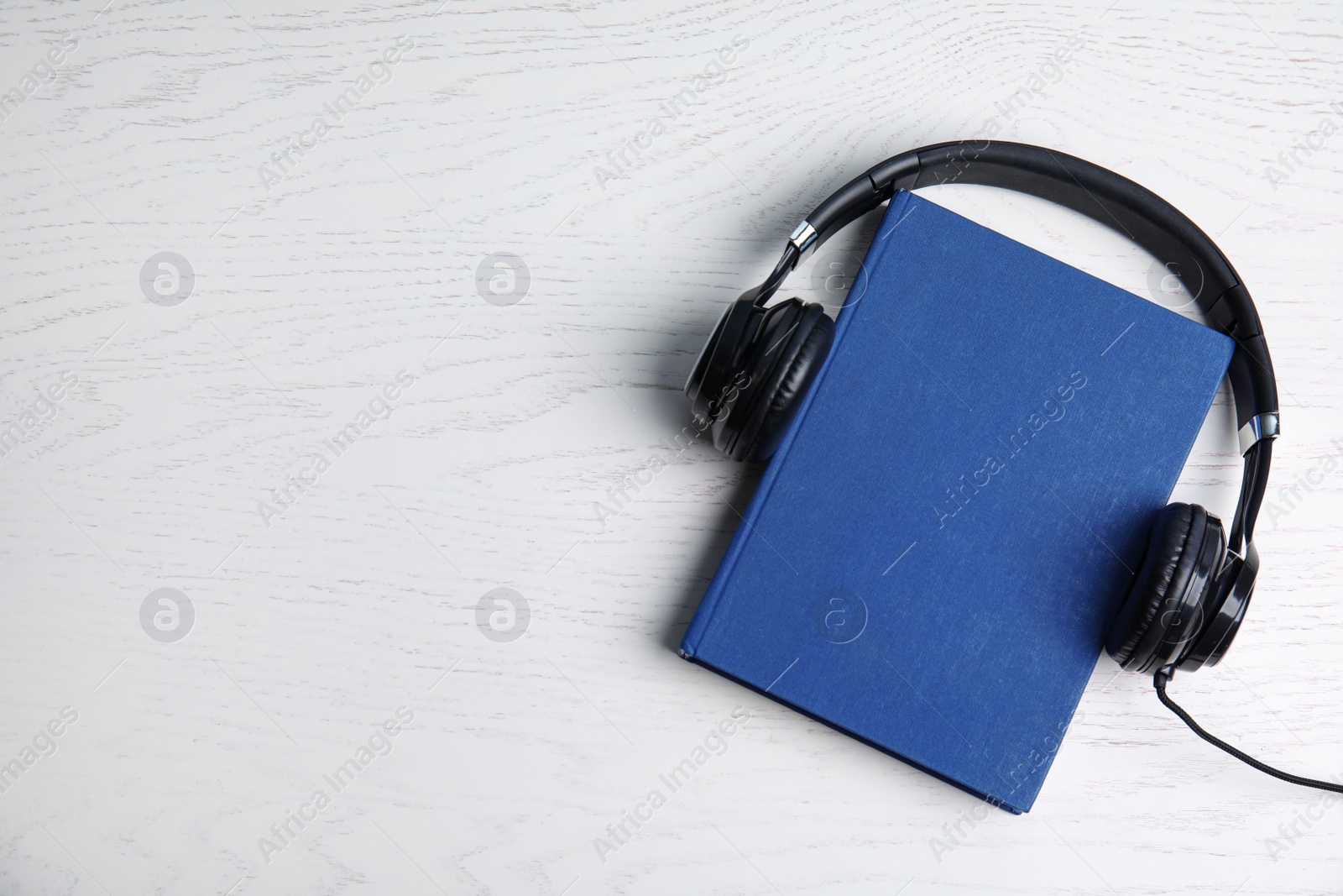 Photo of Modern headphones with hardcover book on white wooden background, top view. Space for text