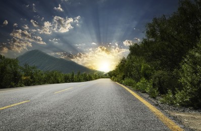 Empty asphalt road, trees and mountains at beautiful sunset