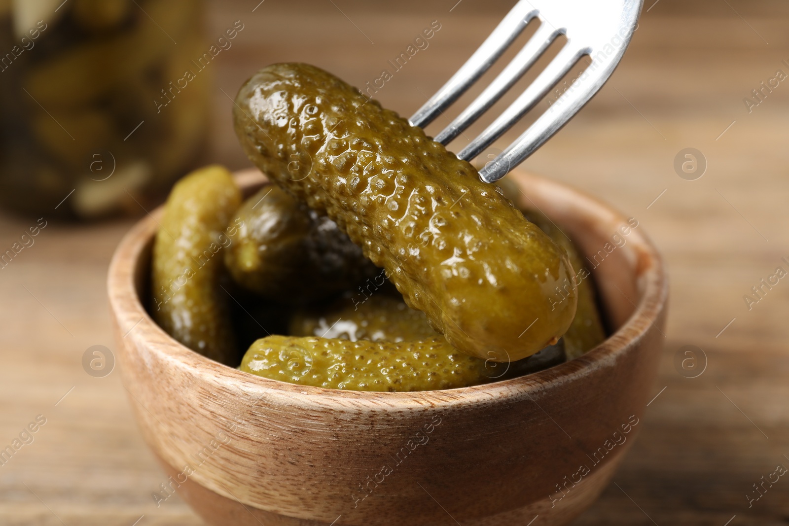 Photo of Eating tasty pickled cucumber from bowl at table, closeup