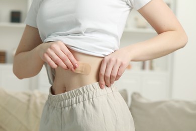 Photo of Woman applying contraceptive patch onto her body indoors, closeup