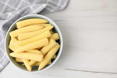 Photo of Tasty fresh yellow baby corns in bowl on white wooden table, top view. Space for text