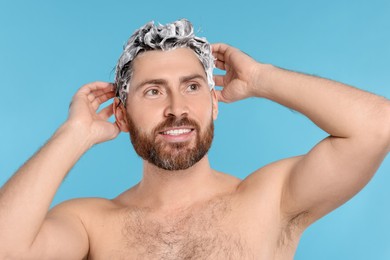 Happy man washing his hair with shampoo on light blue background