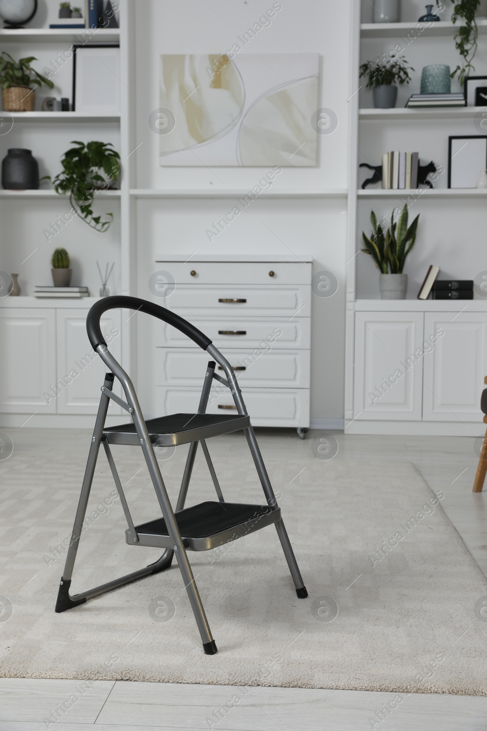 Photo of Metal folding ladder on soft carpet in stylish room