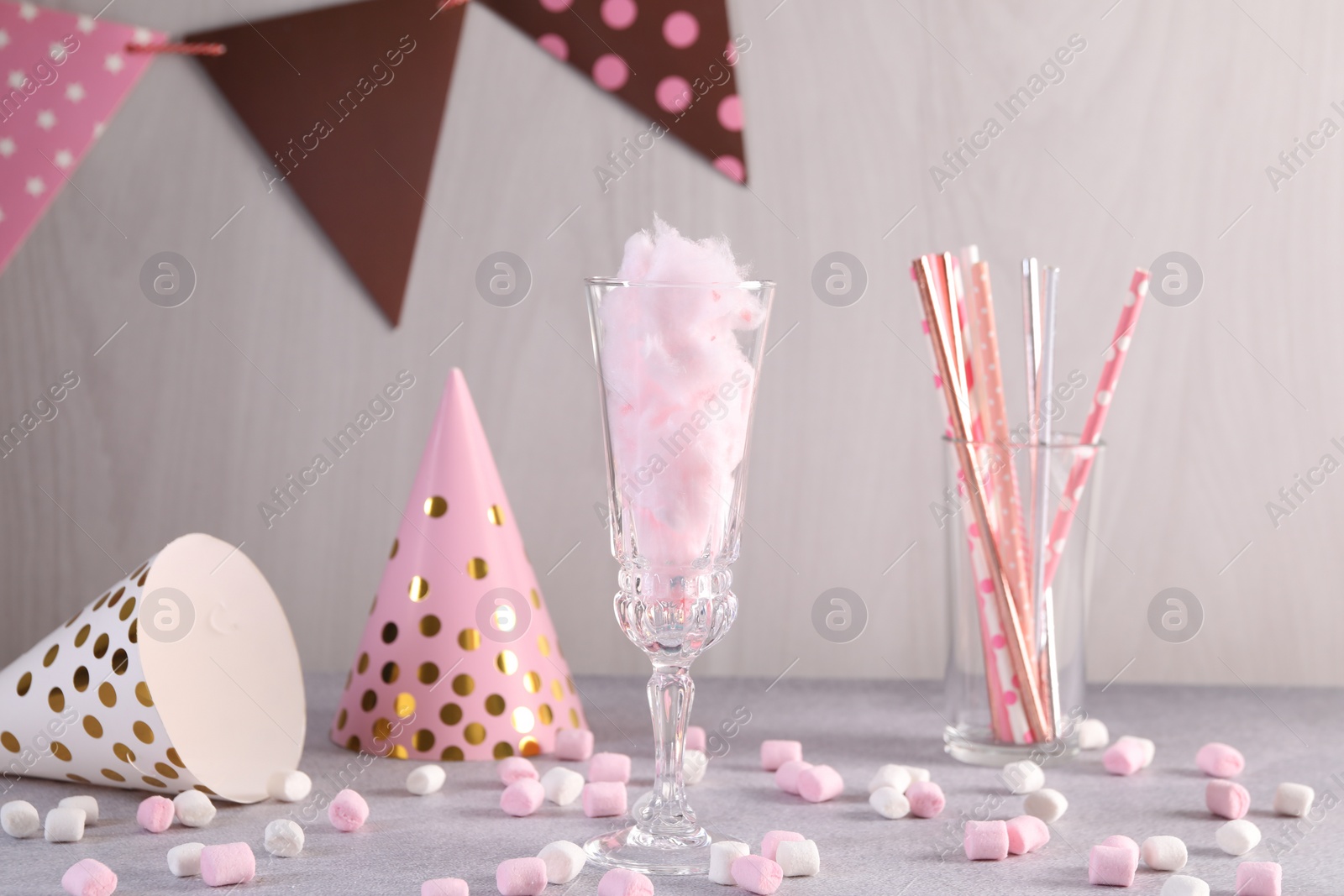 Photo of Tasty cotton candy cocktail in glass, festive decor and marshmallows on gray table against light wooden wall