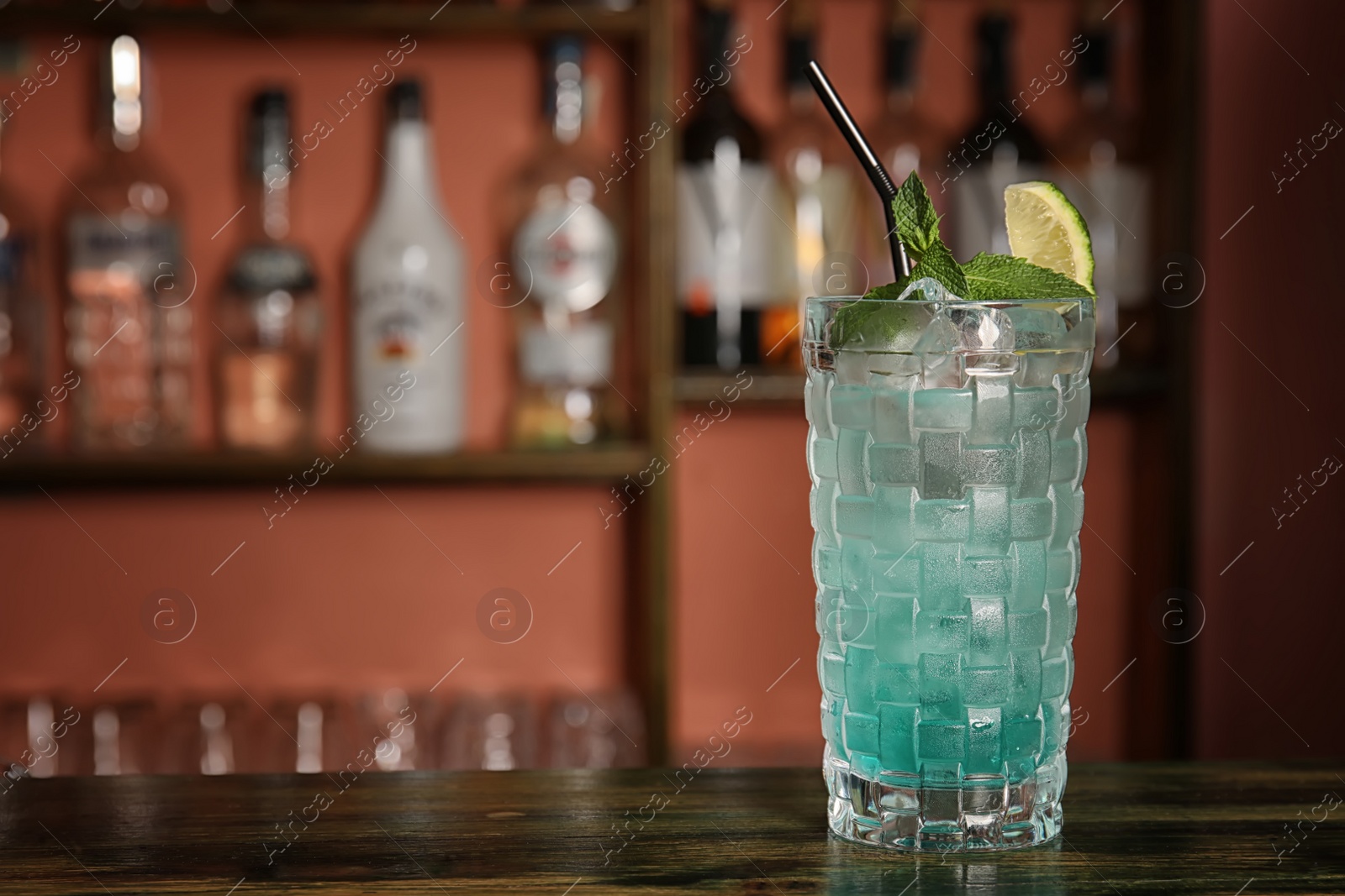 Photo of Glass with delicious cocktail and ice cubes on counter in bar