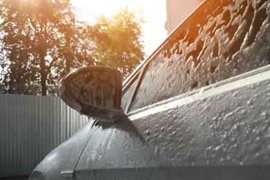 Photo of Auto with cleaning foam at outdoor car wash, closeup