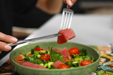 Young woman eating tasty salad with red fish at table, closeup