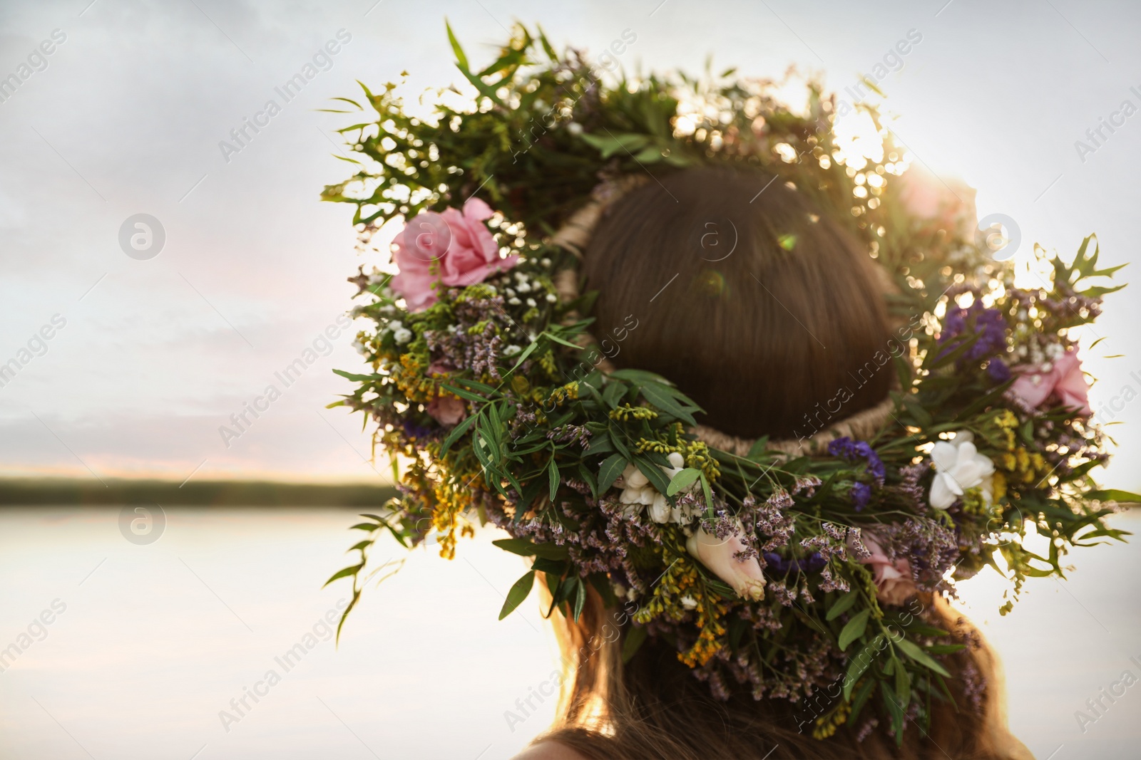 Photo of Young woman wearing wreath made of beautiful flowers near river, closeup