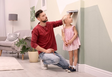 Young man measuring his daughter's height at home