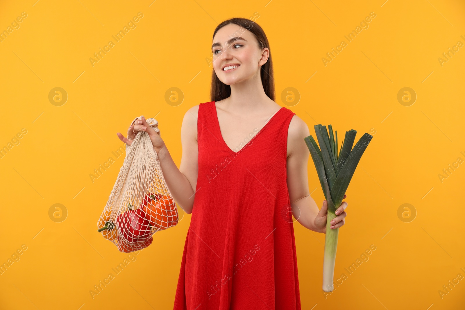 Photo of Woman with string bag of fresh vegetables on orange background