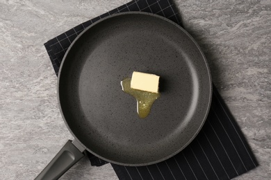 Frying pan with melting butter on grey table, top view