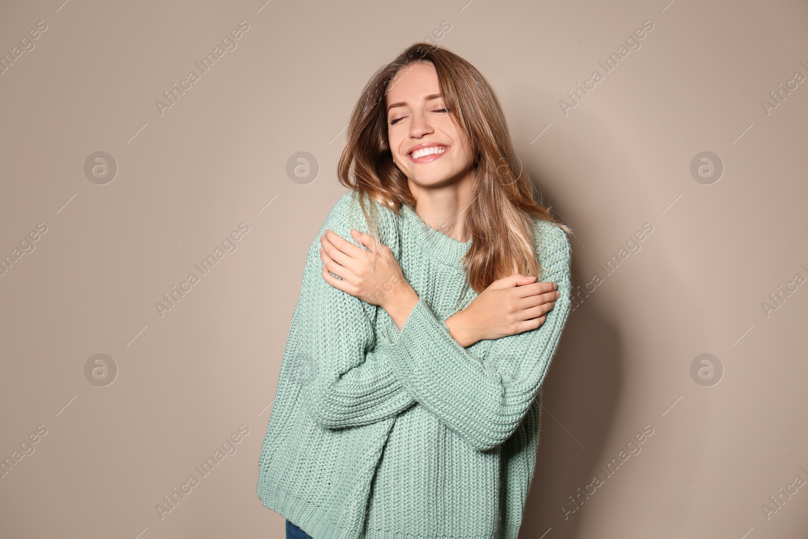 Image of Happy young woman wearing warm sweater on beige background 