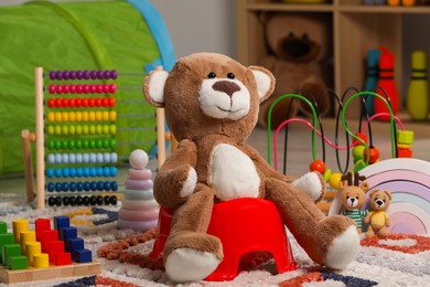 Photo of Teddy bear on red baby potty and toys in room. Toilet training